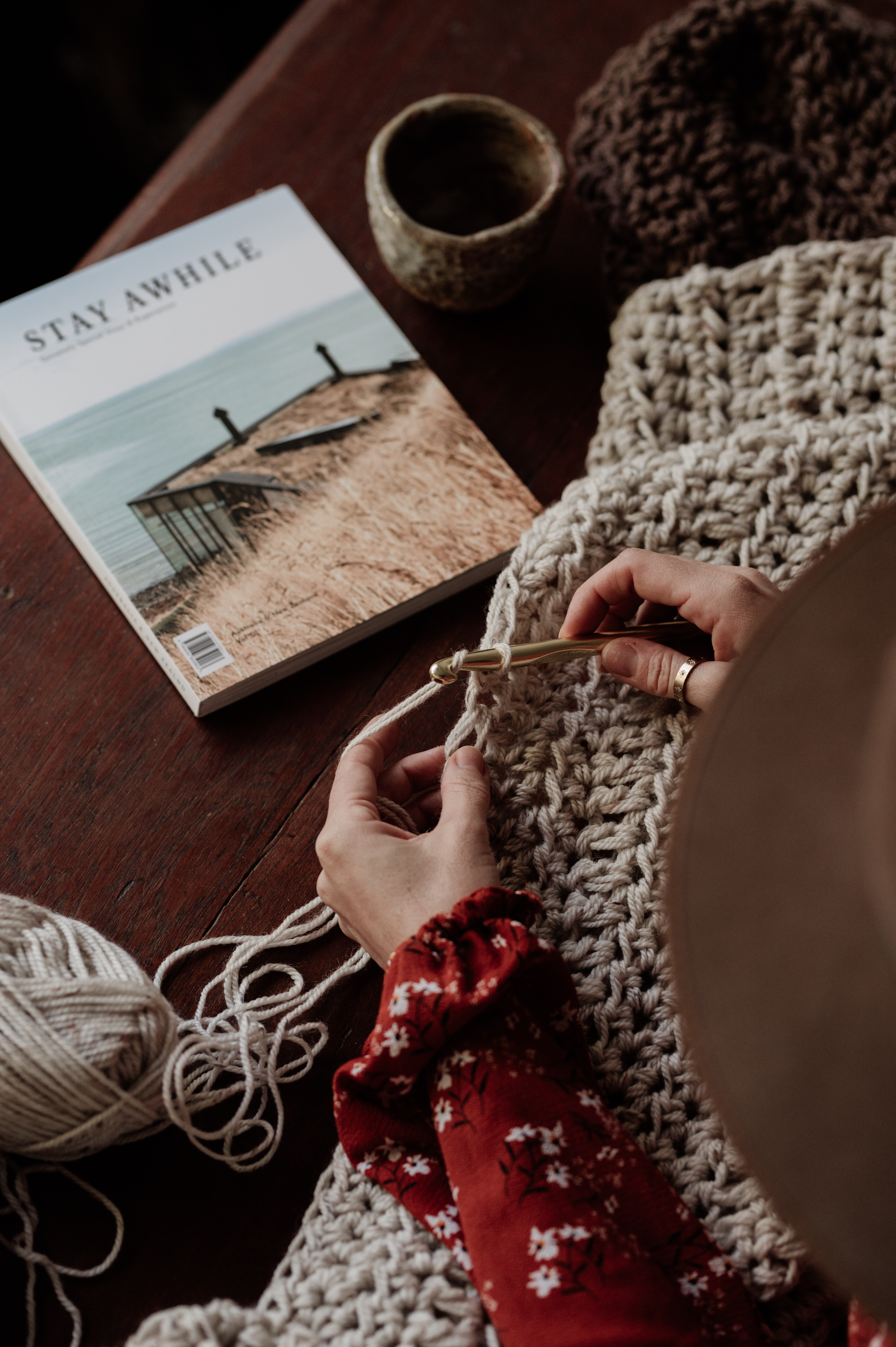 a picture of a lady knitting a wool blanket with a book next to her .
