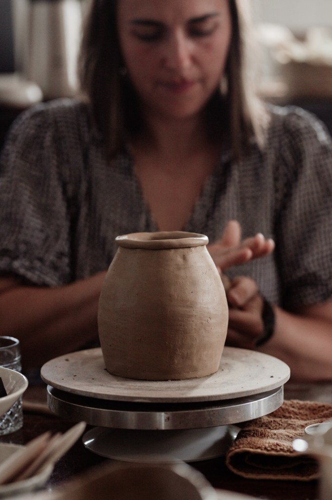 a lady sitting in a moody room working with her hands making clay 